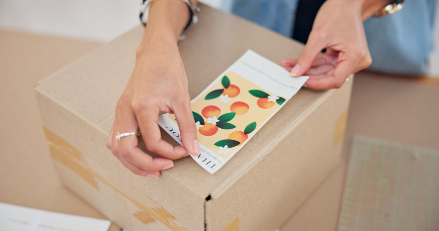 Impression M rectangular sticker with orange fruit pattern being applied to a cardboard shipping box